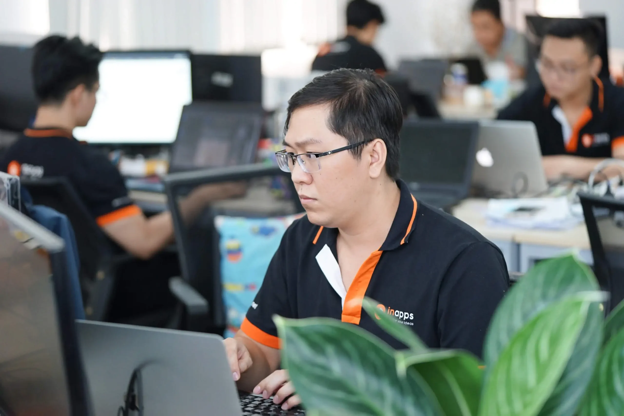 An InApps engineer working at a laptop in the open-plan Ho Chi Minh City office, with colleagues at their desks behind him