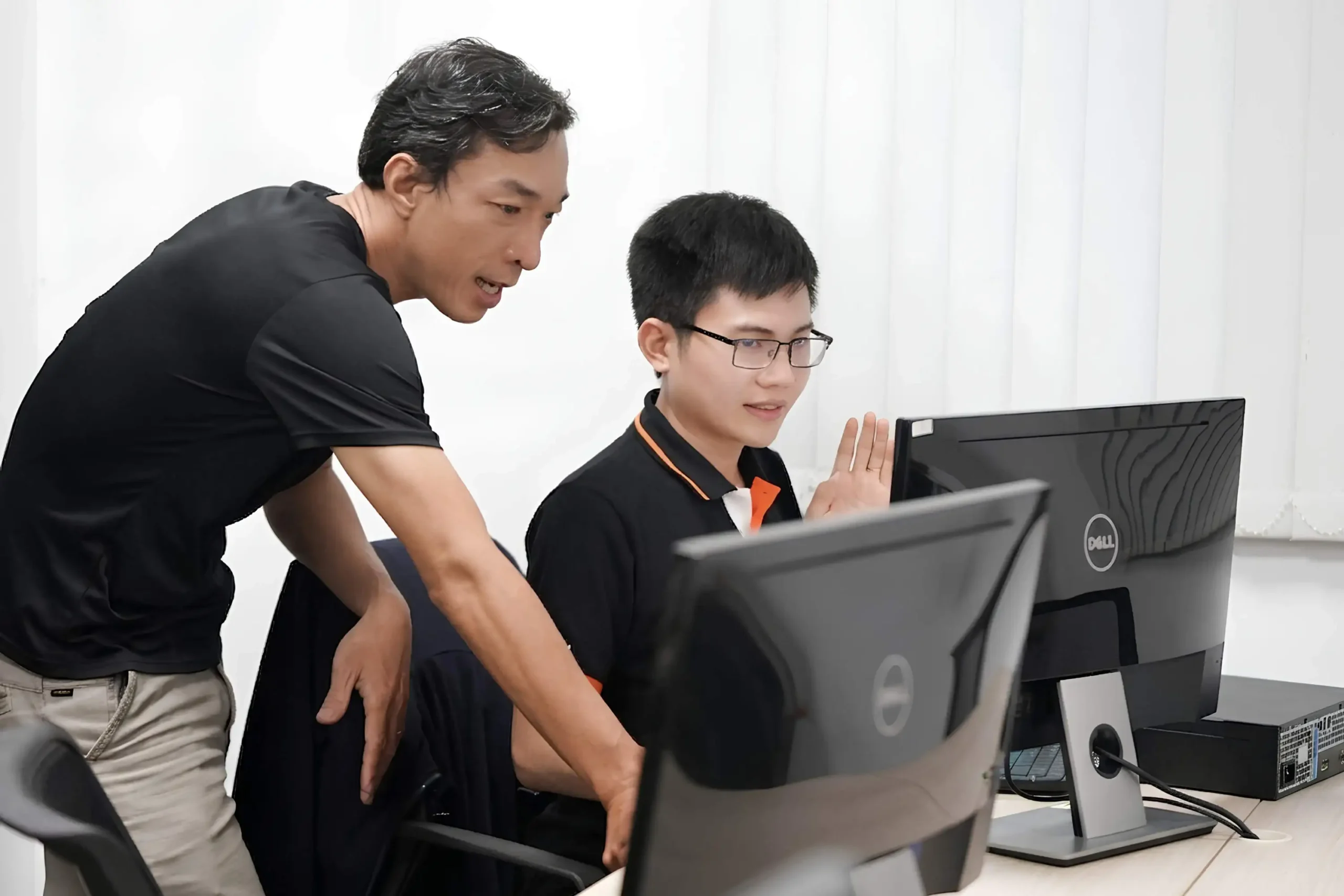 Two InApps engineers at a desk in the Ho Chi Minh City office, one leaning in while the other gestures at what is on the monitor